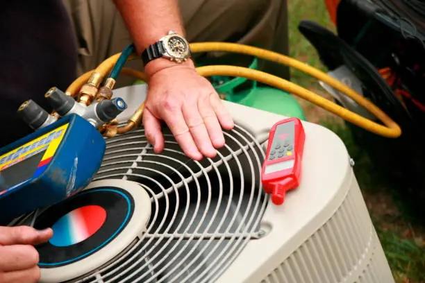 HVAC technician using gauges to service an outdoor air conditioning unit
