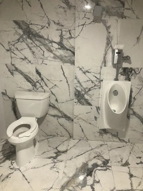 Commercial restroom plumbing fixtures, toilet and wall-mounted urinal, in a marble-tiled bathroom