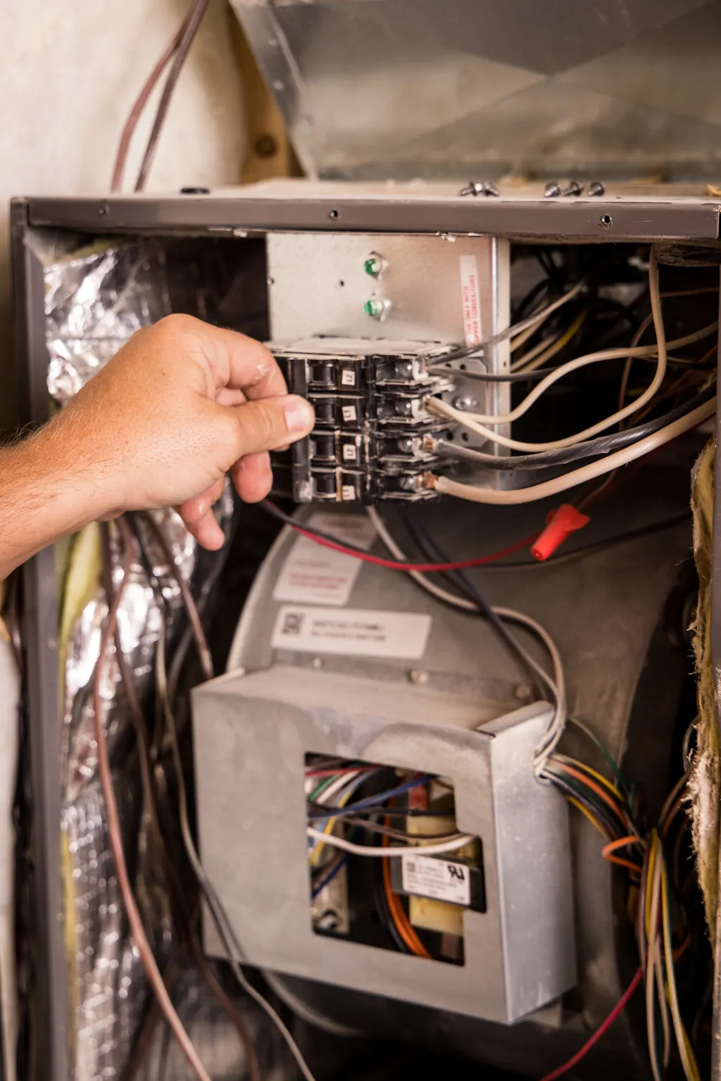 Technician repairing the electrical control panel inside a furnace during an emergency heating call