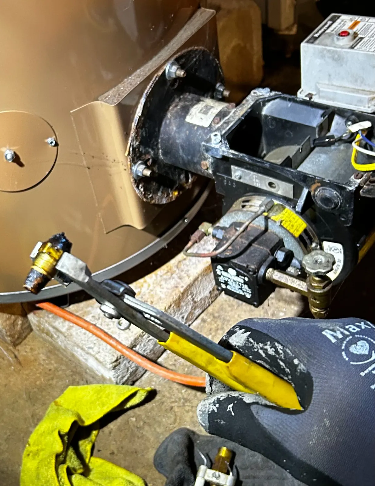Close-up of a Proto Home Service technician using a wrench to service an oil burner assembly on a residential heating system.